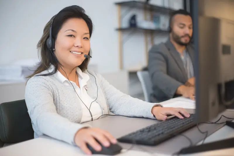 Two dispatchers with headsets at their desks, one smiling while she books a call