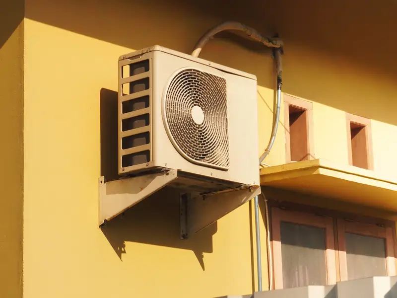 Heat pump mounted on a yellow stucco wall