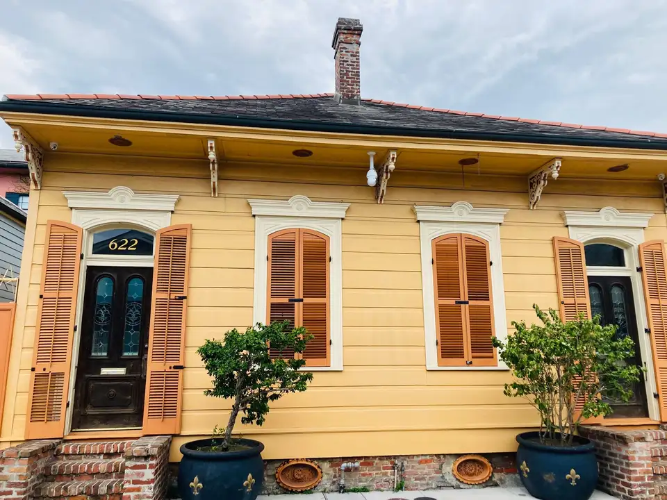 Yellow Creole cottage with tall shutters and potted plants on a New Orleans street