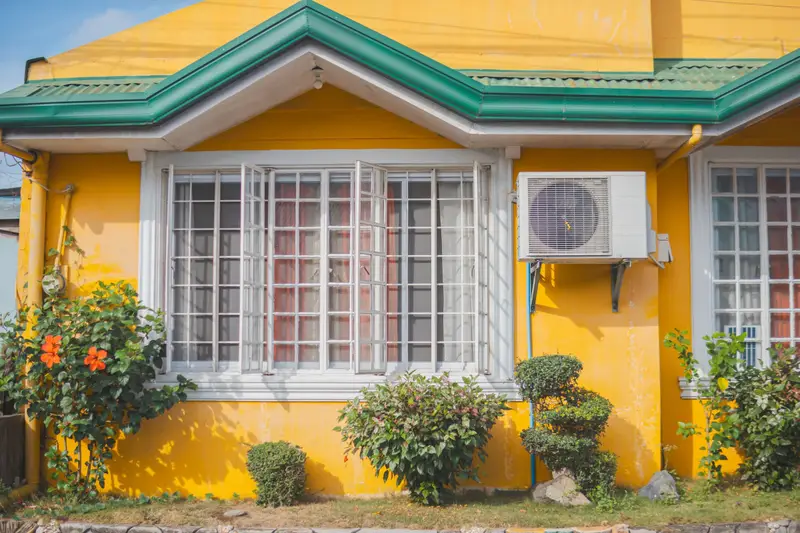 Clean outdoor unit mounted on the wall of a bright yellow house