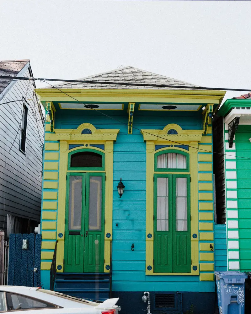Teal and green shotgun house with tall shuttered doors